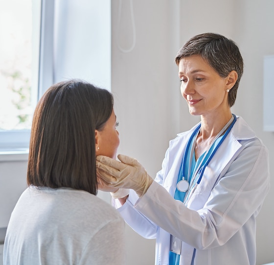 Middle-aged woman doctor wearing gloves checking patients sore throat or thyroid glands